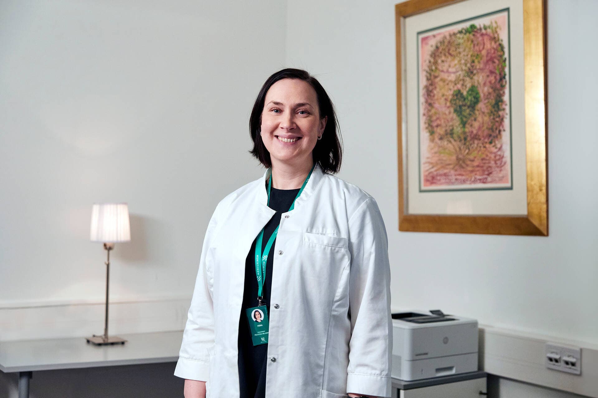 Mehiläinens gynekolog ler och står framför en färgglad tavla.