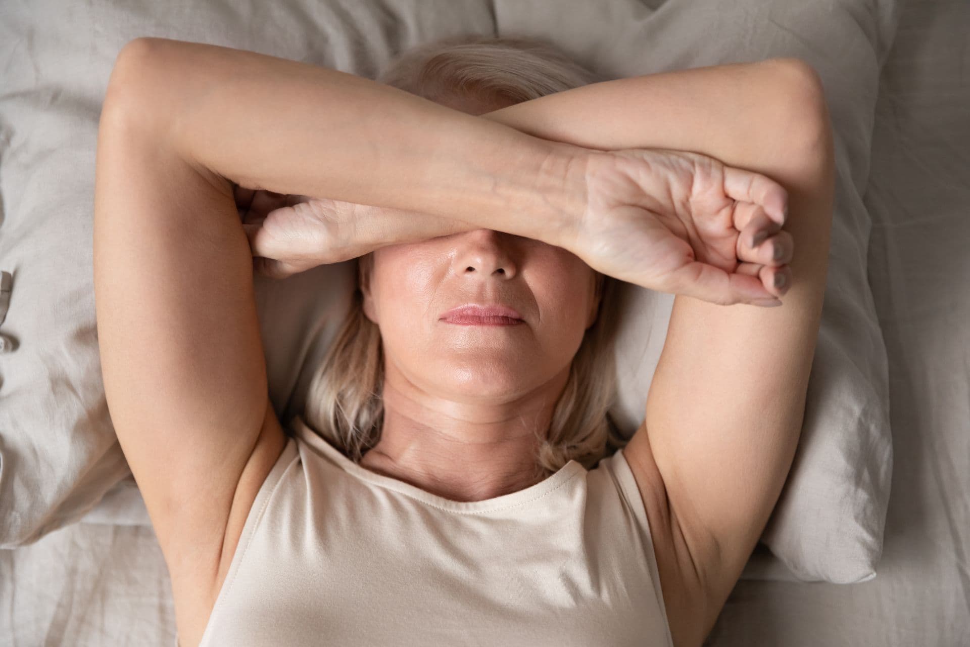A woman suffering from sleep apnea crossed her arms in front of her eyes, lying tiredly in bed.