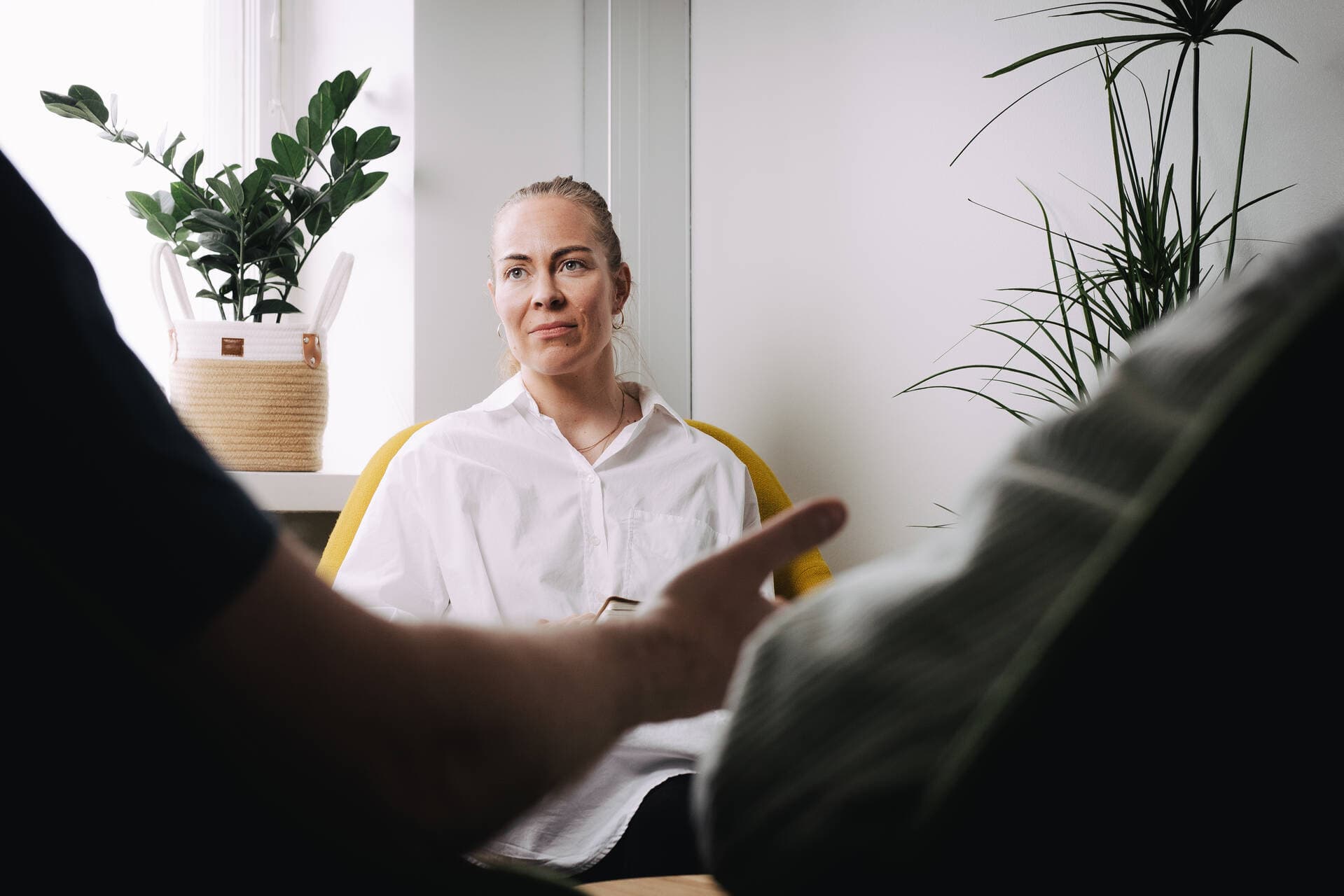 Psykoterapeutti kuuntelee keskittyneenä kahta asiakasta ja hänellä on muistiinpanovihko sylissä.