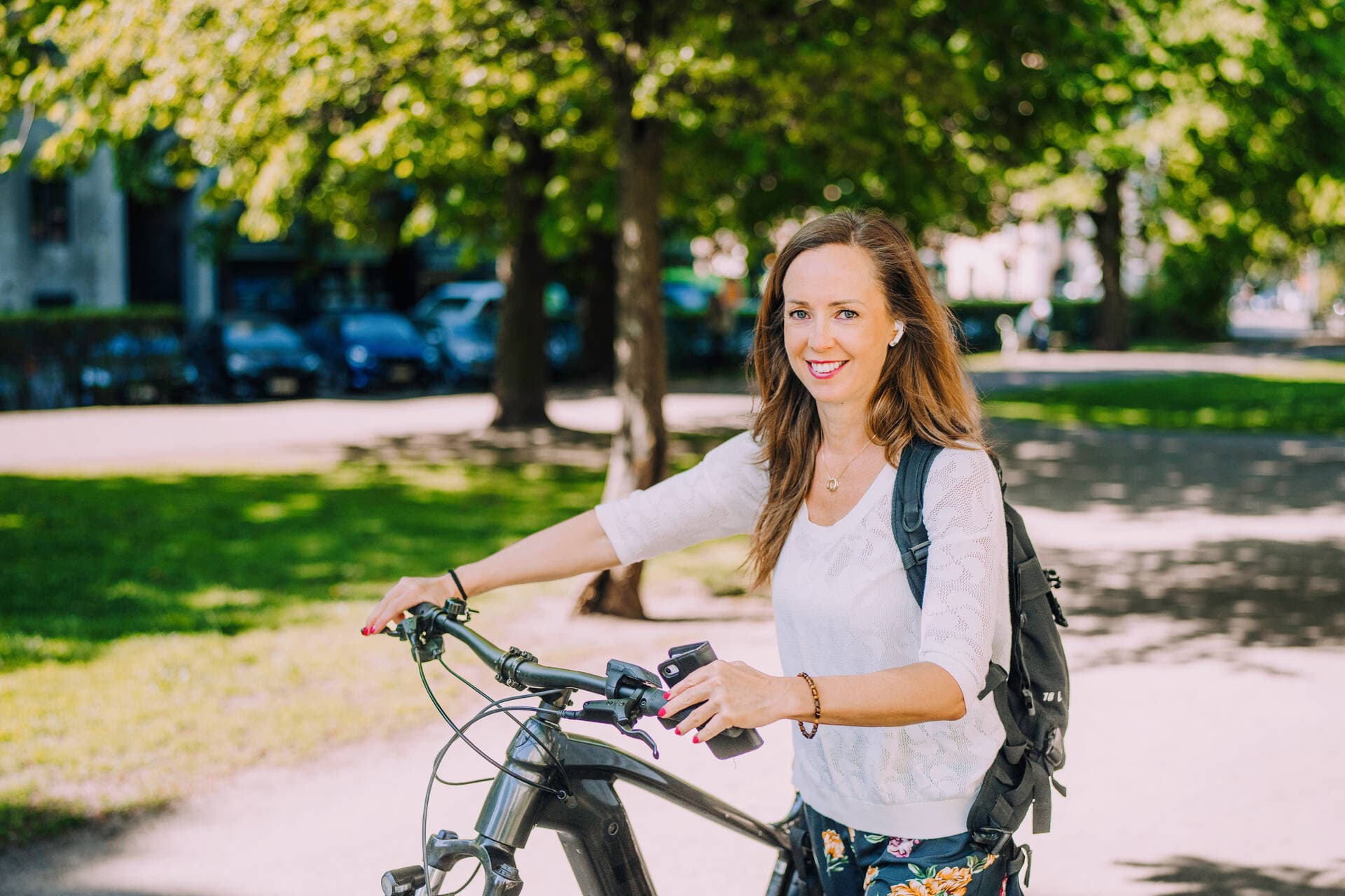 En anställd på Mehiläinen leder sin elcykel genom en somrig park på väg till jobbet.