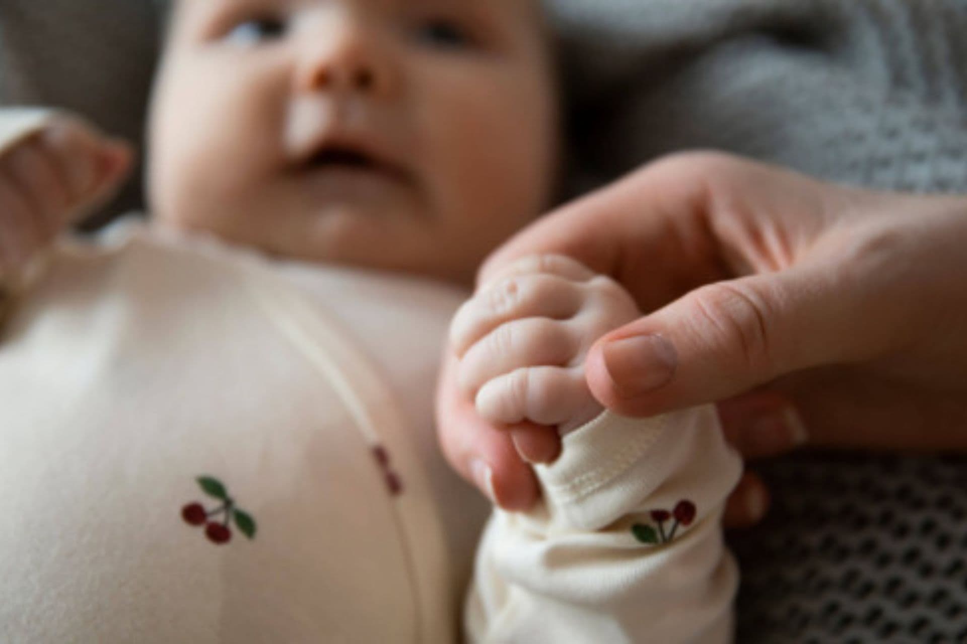 Baby and an adult's hand holding the baby's hand.