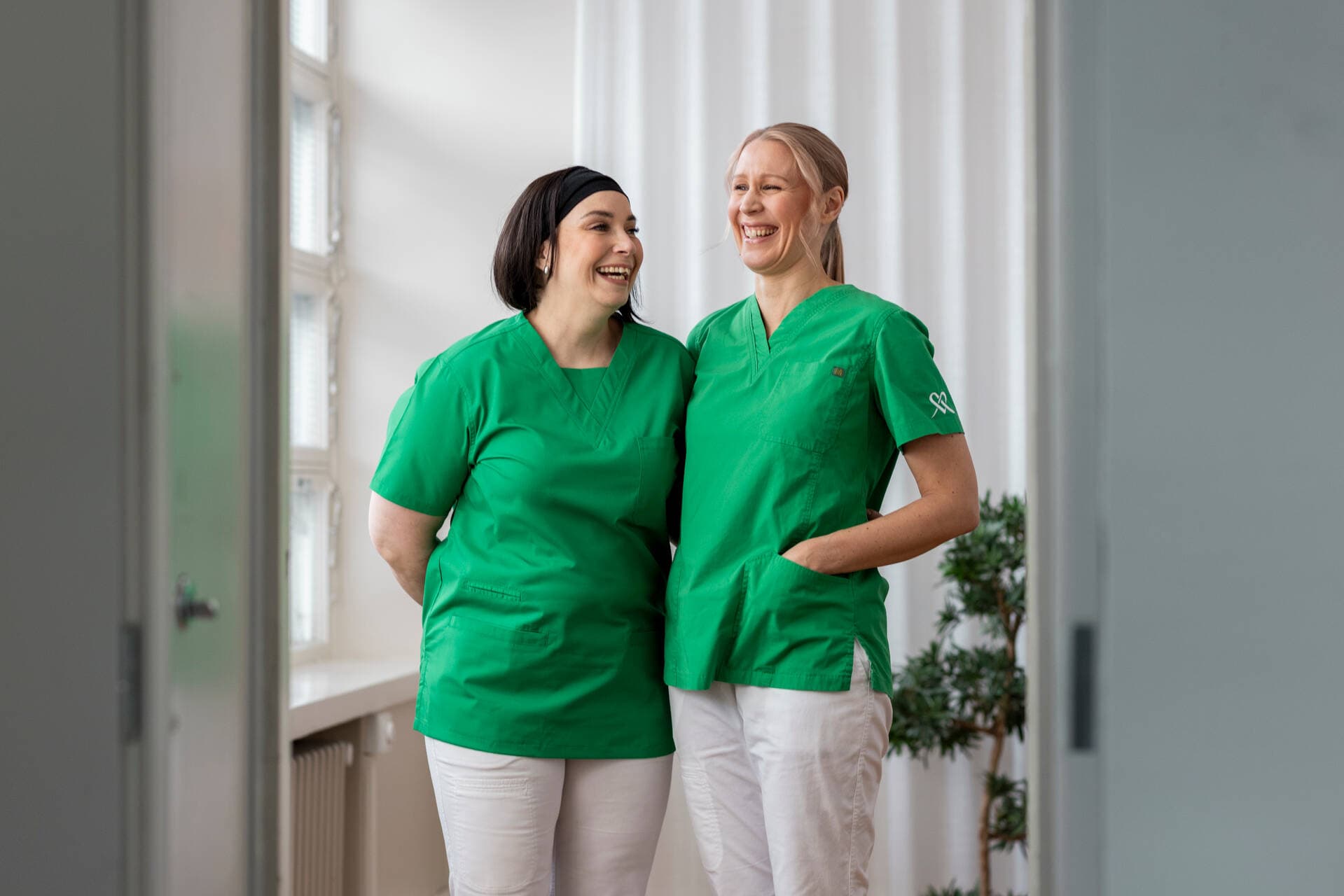 Två sjukskötare på Mehiläinen ler mot varandra.