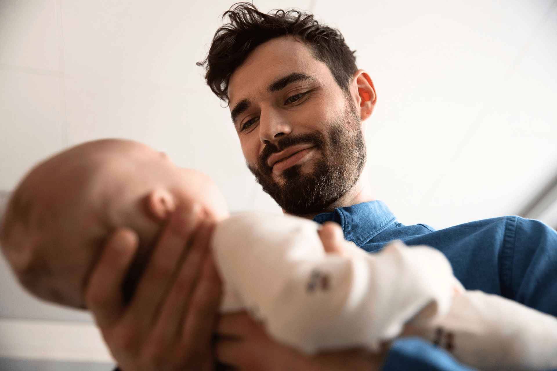 Alhaalta päin kuvattu mies pitelee tyytyväisenä vauvaa käsissään.